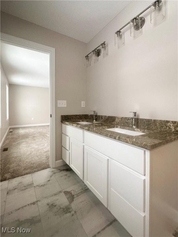 full bath featuring marble finish floor, a sink, baseboards, and double vanity