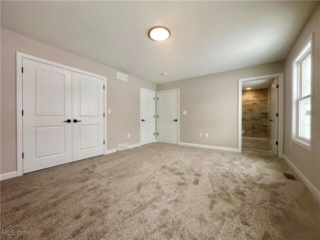 unfurnished bedroom featuring light carpet and ensuite bath