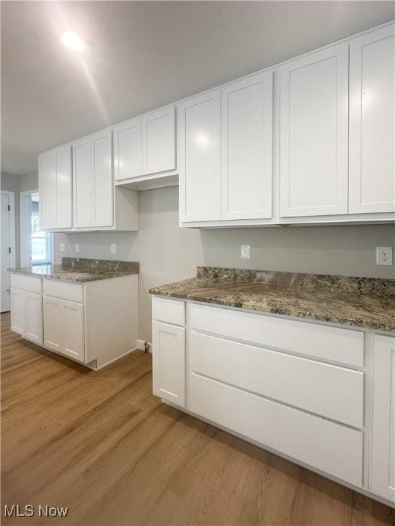 kitchen with light wood-style floors, stone counters, and white cabinets