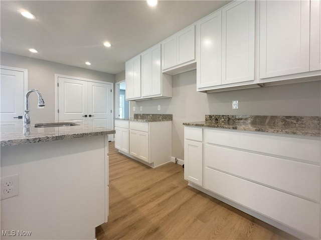 kitchen featuring light stone countertops, sink, white cabinets, and light wood-type flooring