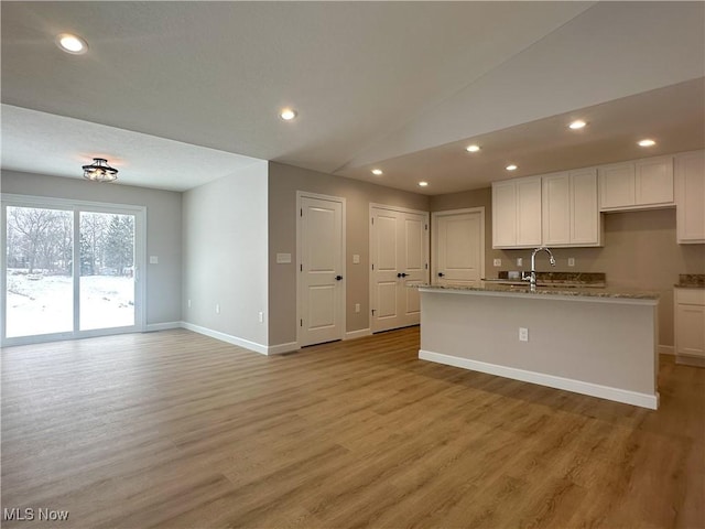 kitchen with lofted ceiling, white cabinetry, and light wood-style floors