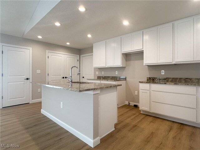 kitchen featuring hardwood / wood-style flooring, an island with sink, sink, and white cabinets