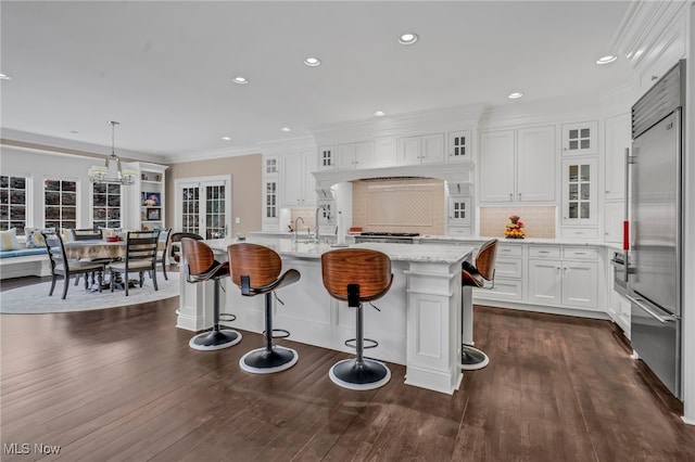 kitchen featuring white cabinetry, light stone countertops, a center island with sink, decorative light fixtures, and built in fridge