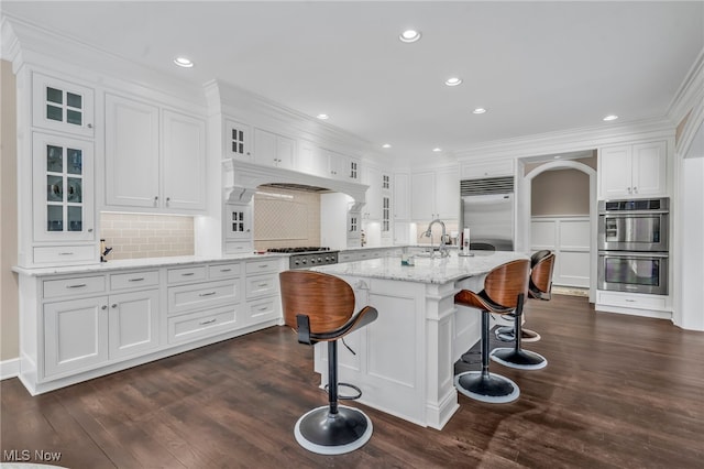 kitchen with stainless steel appliances, white cabinetry, a kitchen island with sink, and light stone counters