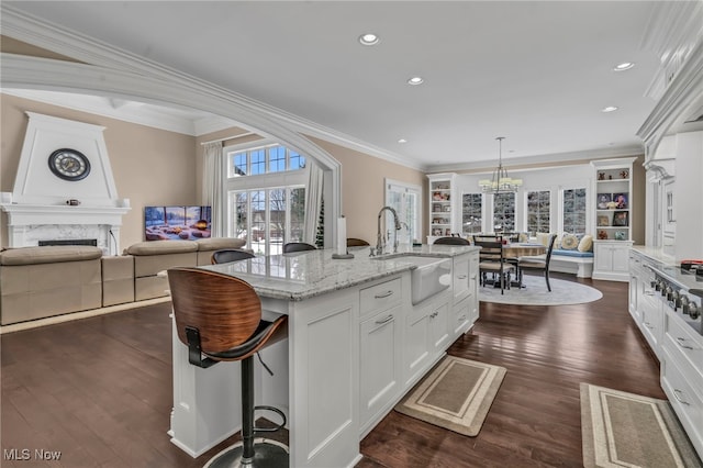 kitchen with decorative light fixtures, an island with sink, sink, white cabinets, and light stone counters