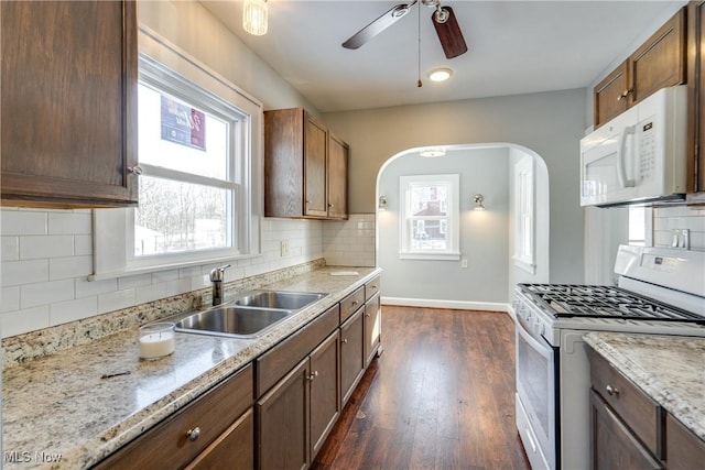 kitchen featuring dark wood-type flooring, sink, light stone counters, white appliances, and decorative backsplash