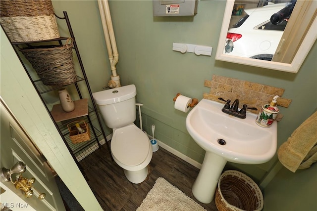 half bath featuring toilet, wood finished floors, baseboards, and a sink