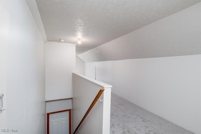 staircase with lofted ceiling, a textured ceiling, and carpet flooring