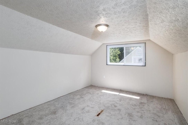 bonus room with lofted ceiling, carpet flooring, and a textured ceiling