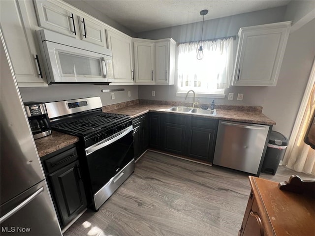 kitchen featuring light wood-style flooring, a sink, stainless steel appliances, white cabinetry, and dark cabinets