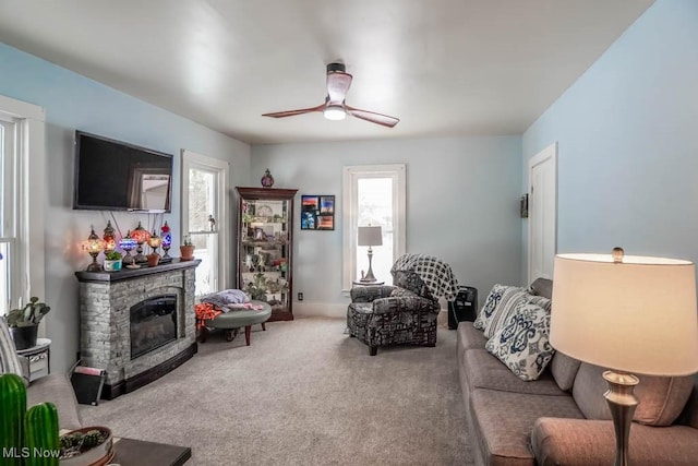 carpeted living room with a stone fireplace, a wealth of natural light, and ceiling fan