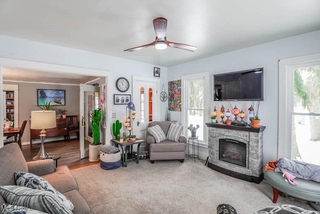 living room featuring plenty of natural light, hardwood / wood-style floors, a stone fireplace, and ceiling fan