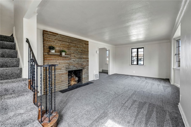 unfurnished living room with dark colored carpet, a stone fireplace, and a textured ceiling