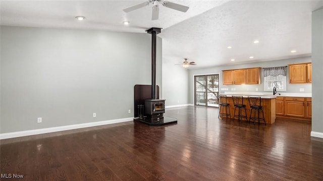 unfurnished living room featuring sink, ceiling fan, a textured ceiling, dark hardwood / wood-style flooring, and a wood stove