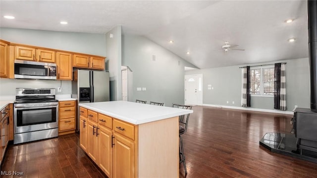 kitchen featuring a center island, a wood stove, appliances with stainless steel finishes, dark hardwood / wood-style floors, and a kitchen breakfast bar