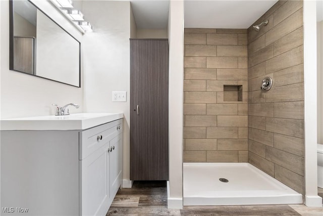 bathroom with vanity, tiled shower, hardwood / wood-style floors, and toilet