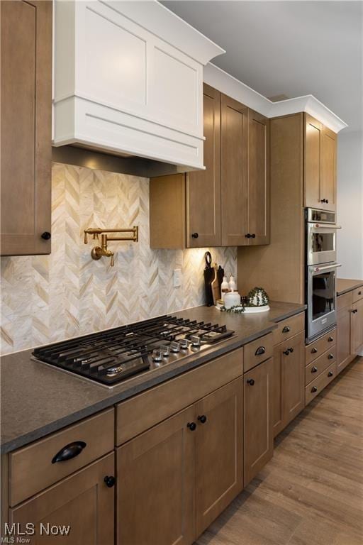 kitchen with ornamental molding, appliances with stainless steel finishes, light hardwood / wood-style flooring, and decorative backsplash