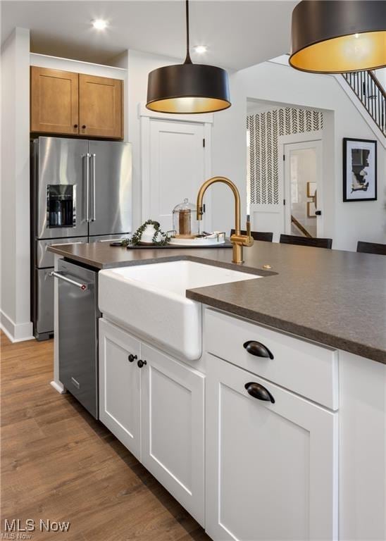 kitchen featuring dark wood-type flooring, sink, decorative light fixtures, appliances with stainless steel finishes, and white cabinets