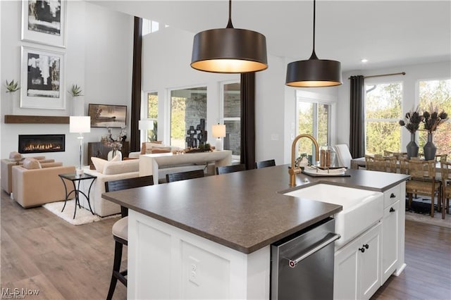 kitchen with pendant lighting, dishwasher, sink, white cabinets, and a center island with sink