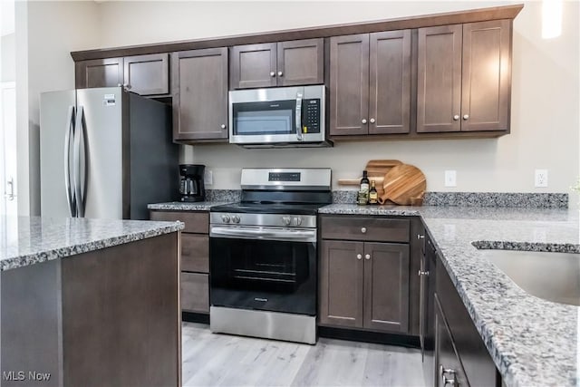 kitchen with light stone counters, dark brown cabinetry, stainless steel appliances, and light hardwood / wood-style floors