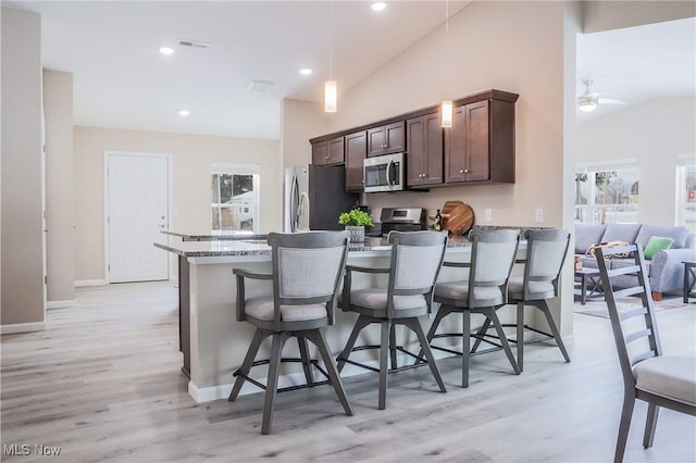 kitchen featuring stainless steel appliances, light stone countertops, a breakfast bar area, and light hardwood / wood-style flooring