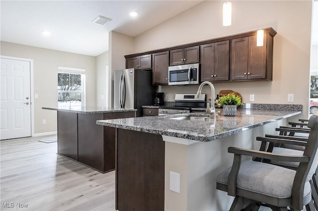 kitchen with dark brown cabinetry, sink, dark stone counters, kitchen peninsula, and stainless steel appliances