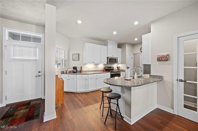 kitchen featuring a kitchen bar, appliances with stainless steel finishes, kitchen peninsula, stone counters, and white cabinets