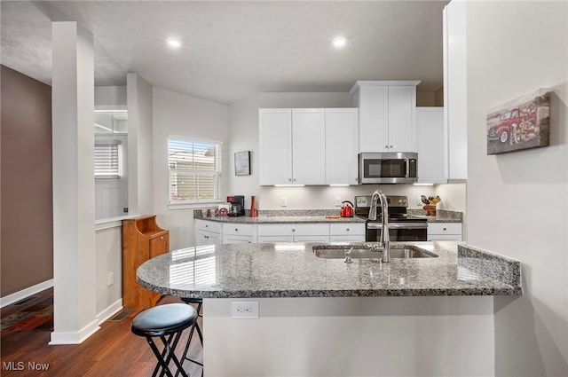 kitchen with stone countertops, sink, white cabinetry, stainless steel appliances, and a kitchen bar