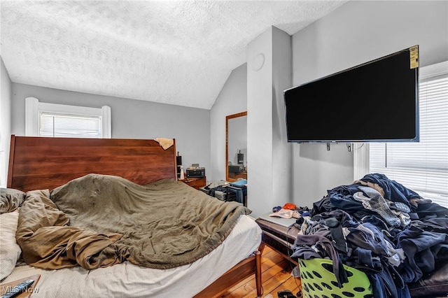 bedroom with multiple windows, vaulted ceiling, hardwood / wood-style flooring, and a textured ceiling