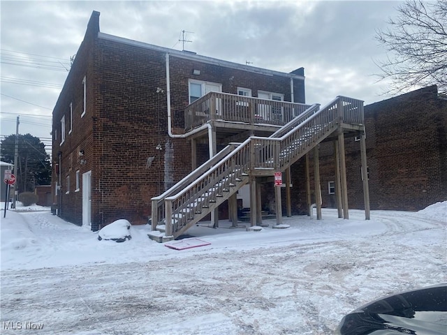 snow covered back of property with a balcony and a deck