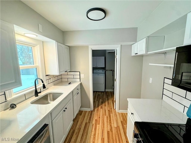 kitchen featuring washer / dryer, sink, light wood-type flooring, white cabinets, and backsplash