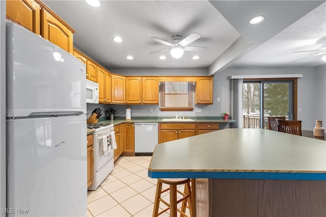 kitchen with sink, white appliances, light tile patterned floors, ceiling fan, and a kitchen breakfast bar