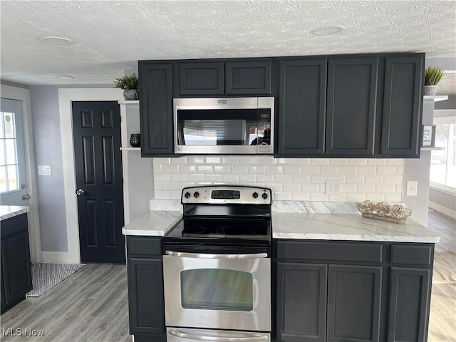 kitchen featuring decorative backsplash, light wood-type flooring, a textured ceiling, and appliances with stainless steel finishes