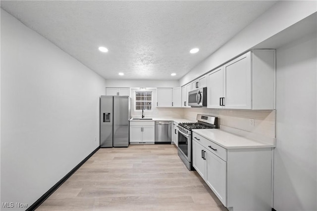 kitchen with appliances with stainless steel finishes, tasteful backsplash, sink, white cabinets, and light hardwood / wood-style flooring