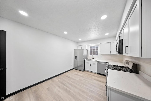 kitchen featuring sink, light hardwood / wood-style flooring, white cabinets, stainless steel appliances, and backsplash