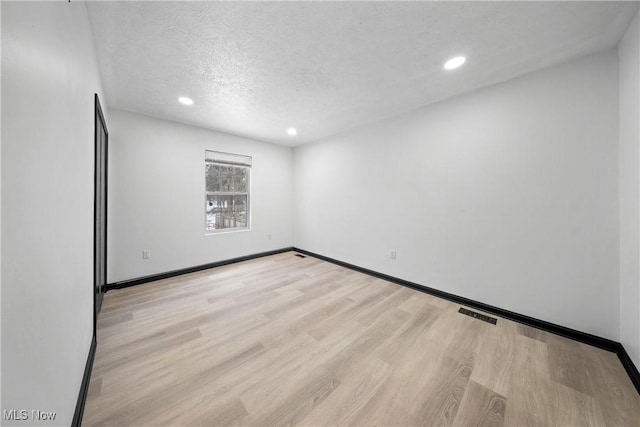 spare room featuring a textured ceiling and light hardwood / wood-style flooring