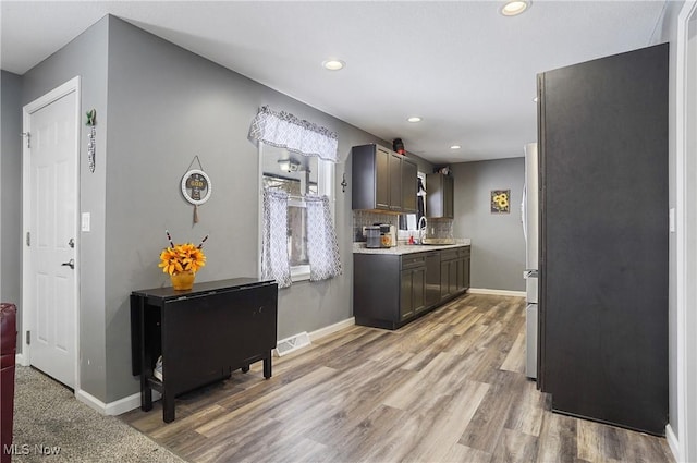 kitchen featuring dark brown cabinetry, sink, decorative backsplash, and light wood-type flooring