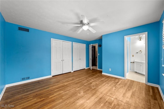 unfurnished bedroom with two closets, light wood-type flooring, connected bathroom, and ceiling fan