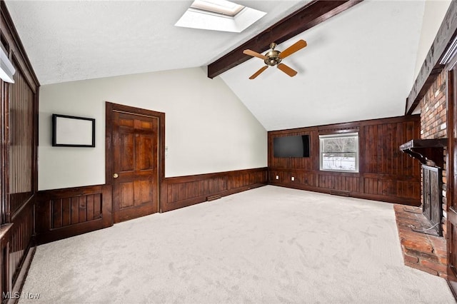 unfurnished living room featuring light carpet, wooden walls, lofted ceiling with skylight, and ceiling fan