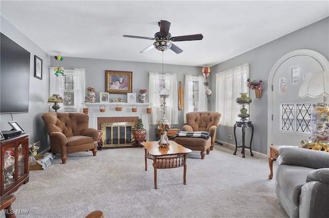 carpeted living room with a brick fireplace, a healthy amount of sunlight, and ceiling fan