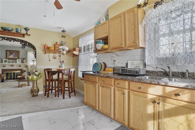 kitchen featuring sink, tasteful backsplash, light carpet, ceiling fan, and a fireplace