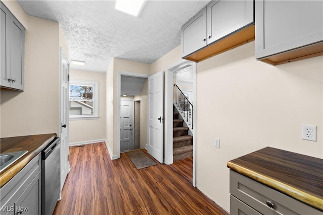 kitchen featuring butcher block countertops, dishwasher, gray cabinetry, dark wood-type flooring, and a textured ceiling