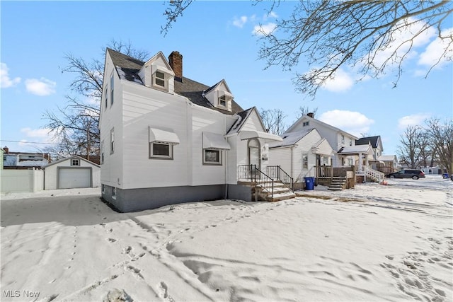 snow covered house featuring a garage and an outbuilding