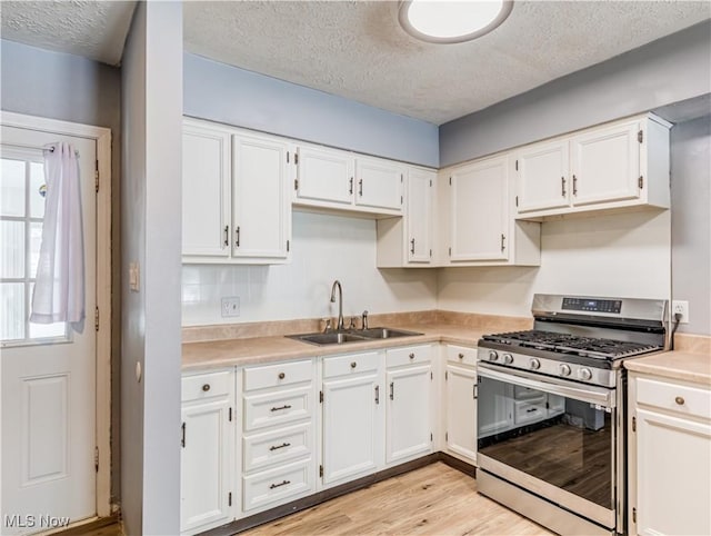 kitchen featuring sink, white cabinets, gas range, a textured ceiling, and light hardwood / wood-style flooring