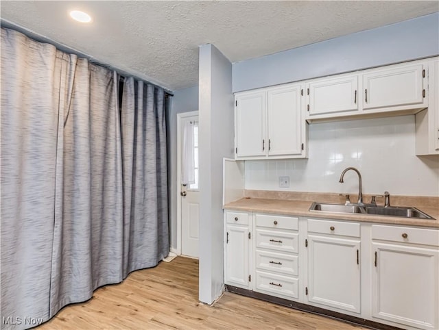 kitchen with light wood-type flooring, sink, a textured ceiling, and white cabinets