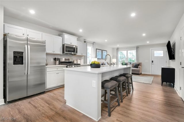 kitchen with appliances with stainless steel finishes, an island with sink, white cabinets, a kitchen bar, and light hardwood / wood-style flooring