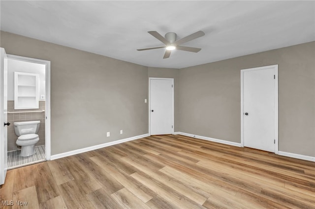 unfurnished bedroom featuring tile walls, light hardwood / wood-style floors, ceiling fan, ensuite bath, and a closet