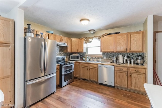 kitchen featuring stainless steel appliances, a textured ceiling, light hardwood / wood-style floors, and decorative backsplash