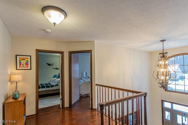 hallway with dark wood-type flooring, a chandelier, and a textured ceiling