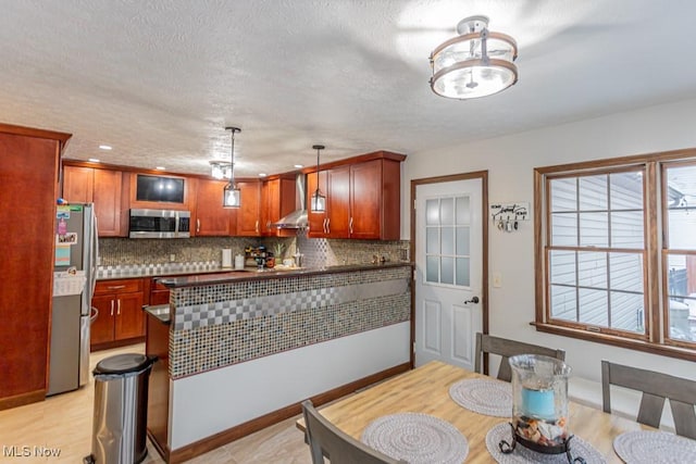 kitchen featuring wall chimney exhaust hood, tasteful backsplash, hanging light fixtures, a textured ceiling, and appliances with stainless steel finishes